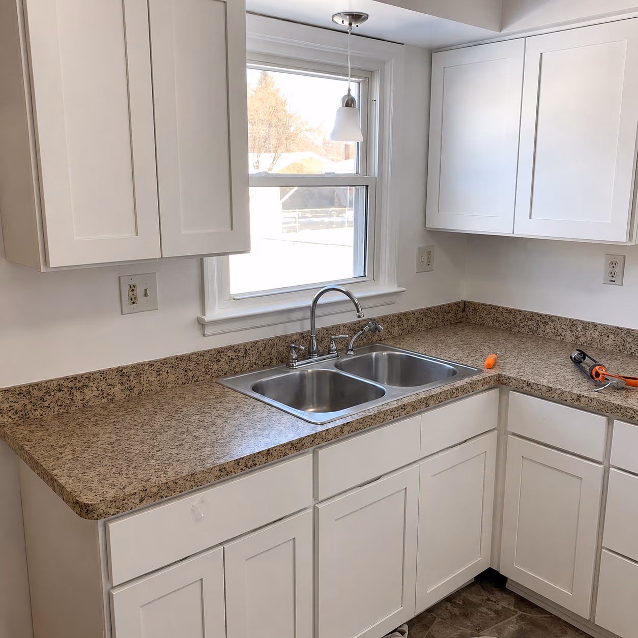 Clean kitchen corner with white cabinets, granite countertop, double stainless steel sink, and window above sink.