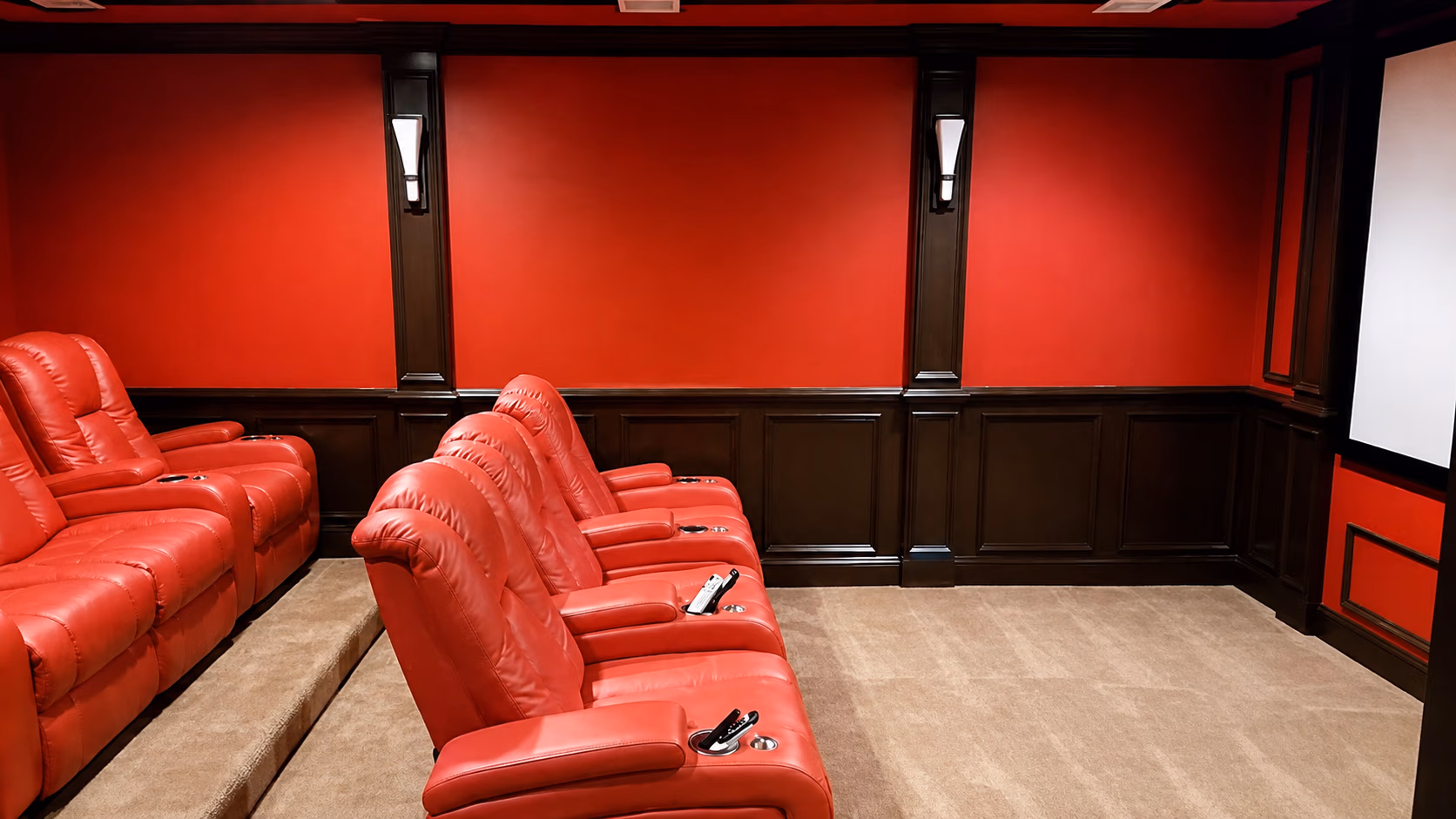 Home theater with red leather recliners facing a large white projector screen and red and dark wood walls.