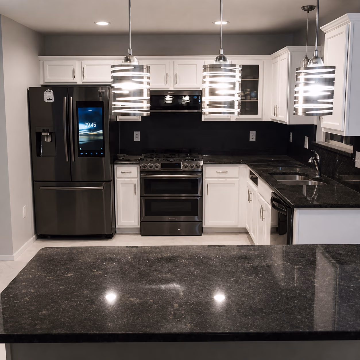 Modern kitchen with black granite countertops, white cabinets, stainless steel appliances, and pendant lights.
