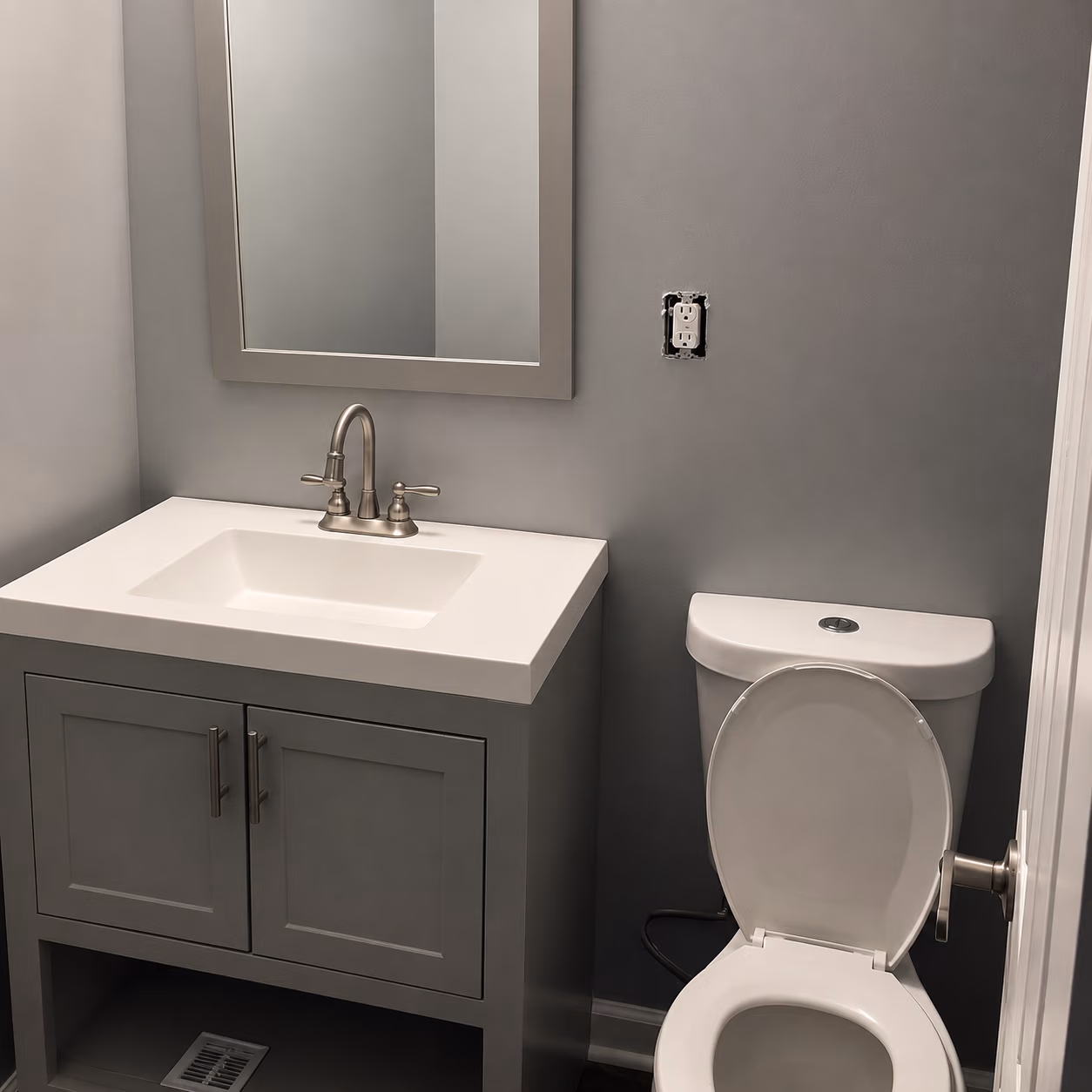 Small bathroom with gray walls, a white sink vanity, and a toilet with an open lid.